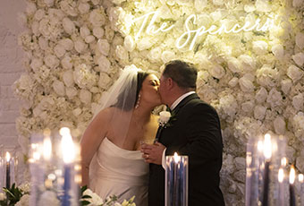 newlyweds kiss in front of custom flower backdrop during reception in Peacock Room at Kimpton Hotel Fontenot