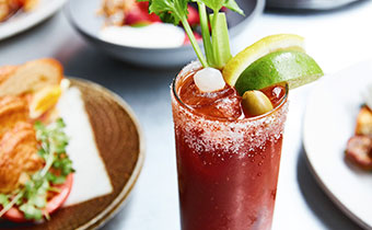 closeup of a bloody mary with brunch dishes in the background