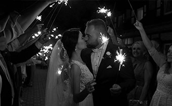 black and white photo of briode and groom kissing as guests hold sparklers